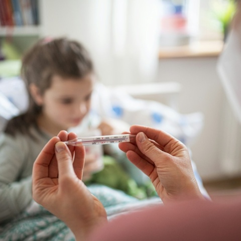 Παιδί με μάσκα και άτομο που του μετρά τη θερμοκρασία