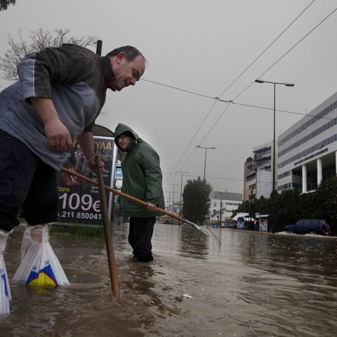 Πολίτες προσπαθούν να καθαρίσουν υπόνομο σε πλημμυρισμένο δρόμο στην Πειραιώς