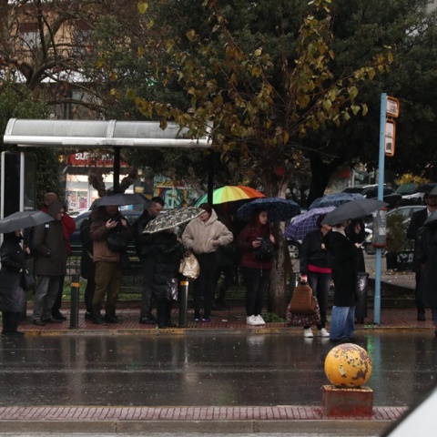Πολίτες σε στάση λεωφορείου περιμένουν έχοντας ανοιχτή την ομπρέλα τους