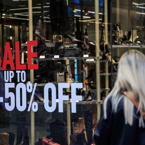 Γυναίκα μπροστά από βιτρίνα με το σήμα των εκπτώσεων