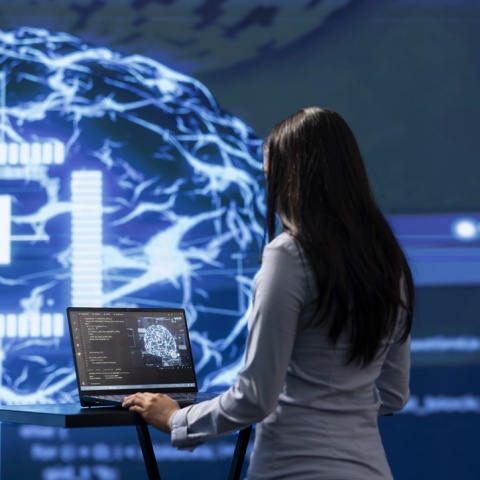 Ερευνήτρια μπροστά από οθόνη που απεικονίζει εγκέφαλο και γράφει τη λέξη ΑΙ