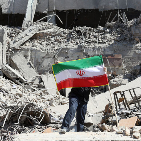 Ένας άντρας βάζει την ιρανική σημαία πάνω στα χαλάσματα βομβαρδισμένου κτιρίου στην Τεχεράνη