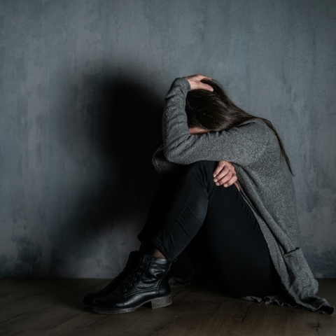 Γυναίκα κρύβει το πρόσωπό της ενώ είναι καθισμένη στο πάτωμα ενός σπιτιού