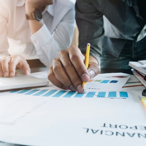 Έγραφα πάνω σε τραπέζι που γράφουν Financial Report και άτομα που τα μελετούν κάνοντας σημειώσεις με μολύβι