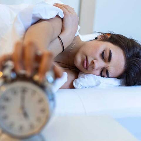 Γυναίκα κοιμάται στο κρεβάτι με φόντο το ξυπνητήρι