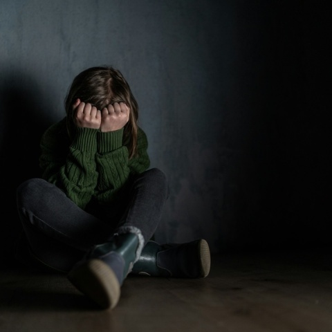 κορίτσι σε σκοτεινό δωμάτιο που κρύβει με τα χέρια του το πρόσωπό του