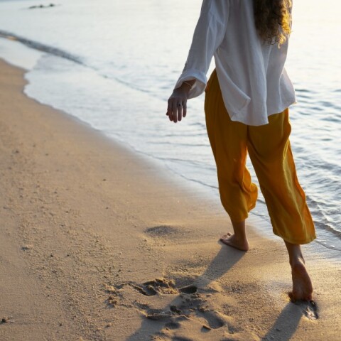 Γυναίκα περπατά ξυπόλυτη στην παραλία