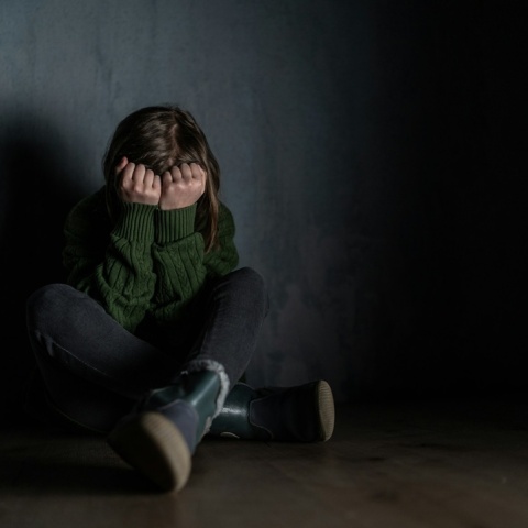 Ανήλικη που κρύβει το πρόσωπό της με τα χέρια της καθισμένη σε ένα σκοτεινό δωμάτιο