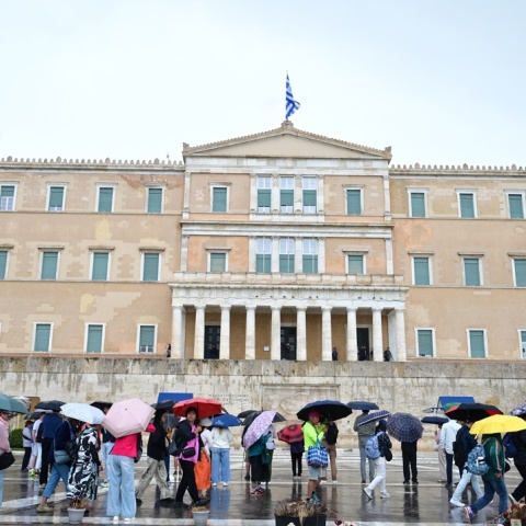 Πολίτες με ομπρέλες εν μέσω βροχής μπροστά από το μνημείο του Άγνωστου Στρατιώτη και τη Βουλή