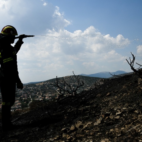 Πυροσβέστης με τη μάνικα ανά χείρας ρίχνει νερό σε καμένο τοπίο
