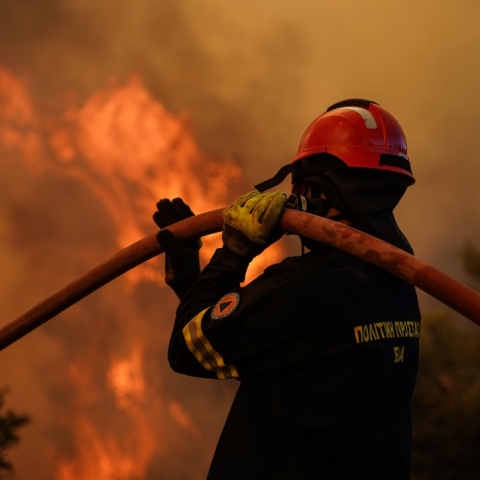 Πυροσβέστης με τη μάνικα στον ώμο και φόντο τις φλόγες