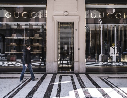 Γυναίκα με μάσκα περπατάει έξω από ένα κλειστό κατάστημα Gucci