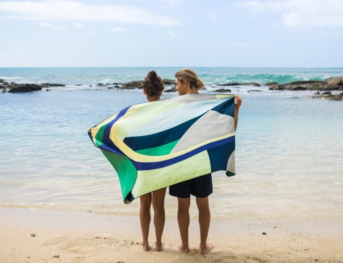 Άντρας και γυναίκα στέκονται με γυρισμένη πλάτη όρθιοι σε παραλία, τυλιγμένοι με μια πετσέτα