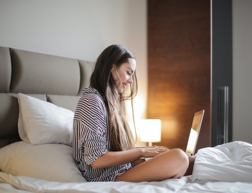 Κοπέλα καθισμένη στο κρεβάτι με ανοιχτό laptop μπροστά της