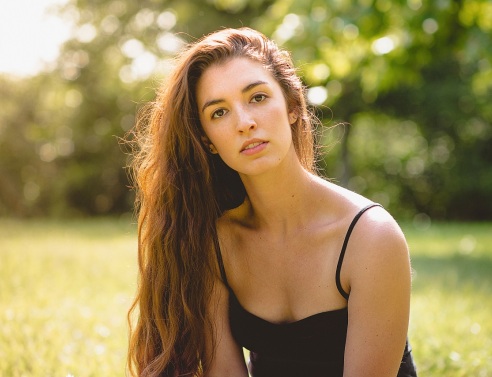 Γυναίκα με μακριά καστανά μαλλιά και μαύρη μπλούζα με τιράντα με φόντο δέντρα