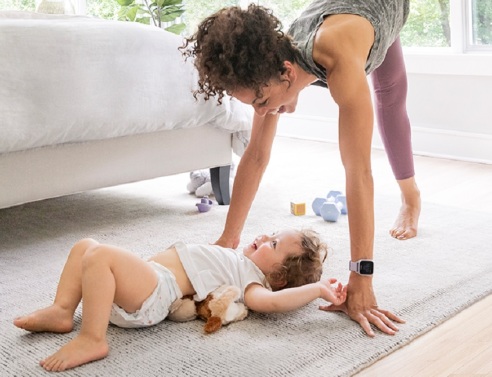 Γυναίκα γυμνάζεται στην κρεβατοκάμαρα δίπλα σε μωρό ξαπλωμένο στο πάτωμα