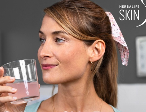 Κοπέλα με μαλλιά αλογοουρά σηκώνει ποτήρι με ροζ υγρό κοντά στο πρόσωπό της