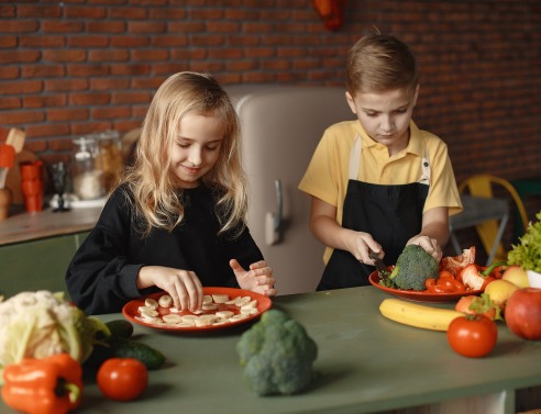Κορίτσι και αγόρι παίζουν με πιάτα φαγητού στο τραπέζι