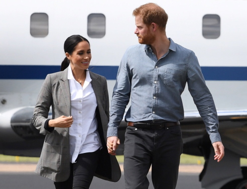 Η Μέγκαν Μαρκλ και ο πρίγκιπας Χάρι περπατούν με φόντο ένα αεροπλάνο