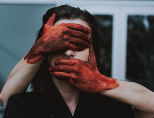 Χέρια με αίματα καλύπτουν πρόσωπο γυναίκας