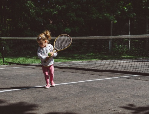 Μικρό κορίτσι σε γήπεδο τένις με μπαλάκι και ρακέτα τένις