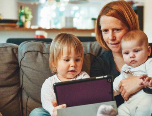 Μια μητέρα κάθεται στον καναπέ αγκαλιά με τα δύο παιδιά της