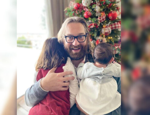 Ο Ευρυπίδης Γουργουλίδης αγκαλιά με τα δύο παιδιά του μπροστά από ένα χριστουγεννιάτικο στολισμένο δέντρο