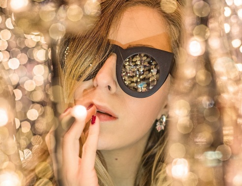 Γυναίκα με γυαλιά ηλίου ανάμεσα σε χρυσά χριστουγεννιάτικα λαμπάκια
