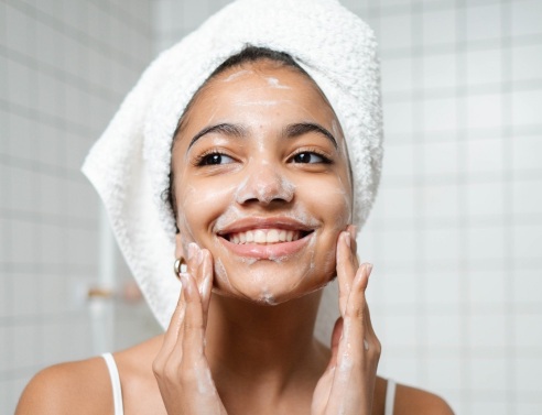 Κοπέλα με πετσέτα στα μαλλιά σαπουνίζει το πρόσωπό της