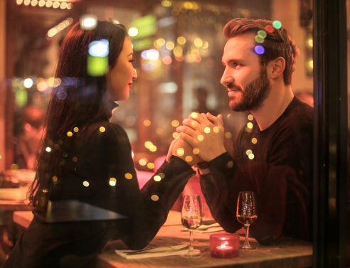 Γυναίκα και άνδρας κρατάνε χέρια καθιστοί σε ένα τραπέζι πίσω από τζαμαρία