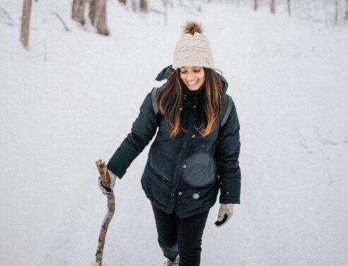 Κοπέλα με μαύρα ρούχα και λευκό σκουφάκι περπατάει στο χιόνι