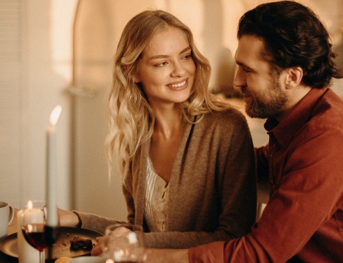 Γυναίκα και άνδρας κοιτάζονται καθισμένοι διπλα δίπλα σε τραπέζι με αναμμένα κεριά