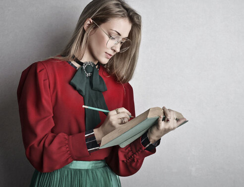 Νεαρή κοπέλα με πράσινη φούστα και κόκκινο πουκάμισο σημειώνει σε βιβλίο