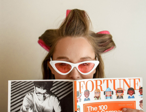 Γυναίκα με ρόλεϊ στα μαλλιά, γυαλιά ηλίου και ανοιγμένο περιοδικό μπροστά στο πρόσωπό της