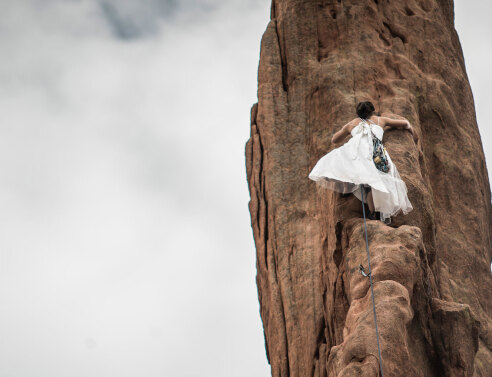 Γυναίκα με λευκό φόρεμα σκαρφαλώνει σε κάθετο βράχο
