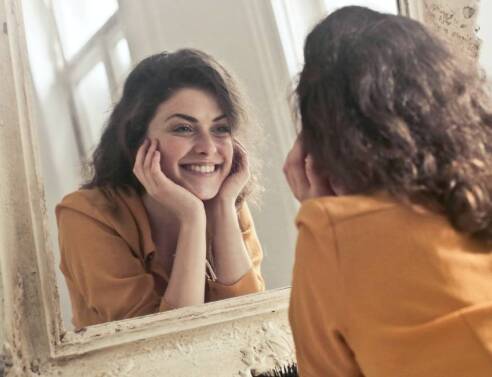 Κοπέλα που κοιτάει στον καθρέφτη και χαμογελάει