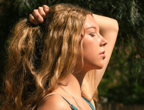 Ξανθιά κοπέλα γυρισμένη προφίλ πιάνει τα μαλλιά της με το ένα χέρι