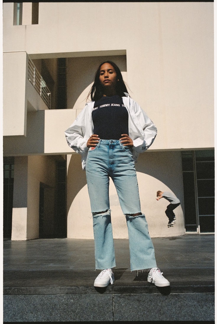 Κοπέλα με τζιν παντελόνι, μαύρη μπλούζα και λευκό μπουφάν ποζάρει