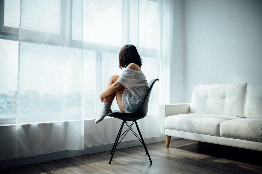 Μελαχρινή γυναίκα καθισμένη σε καρέκλα γυρισμένη προς το παράθυρο
