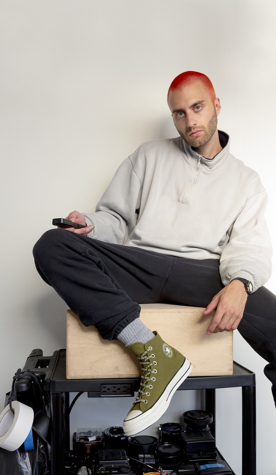 Άνδρας καθισμένος σε ξύλινο κουτί με χακί μποτάκια Converse