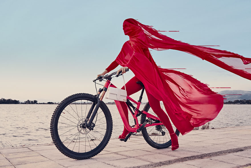 Γυναίκα με κατακόκκινα ρούχα καθισμένη σε ποδήλατο οδηγάει πάνω σε ξύλινη πλατφόρμα