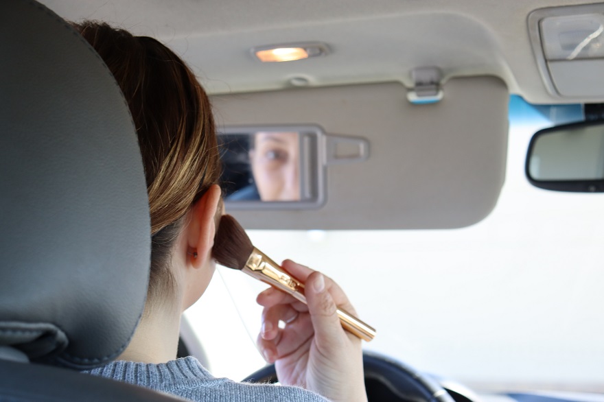 Γυναίκα κοιτιέται στο καθρεφτάκι του αυτοκινήτου και βάζει ρουζ στα μάγουλα