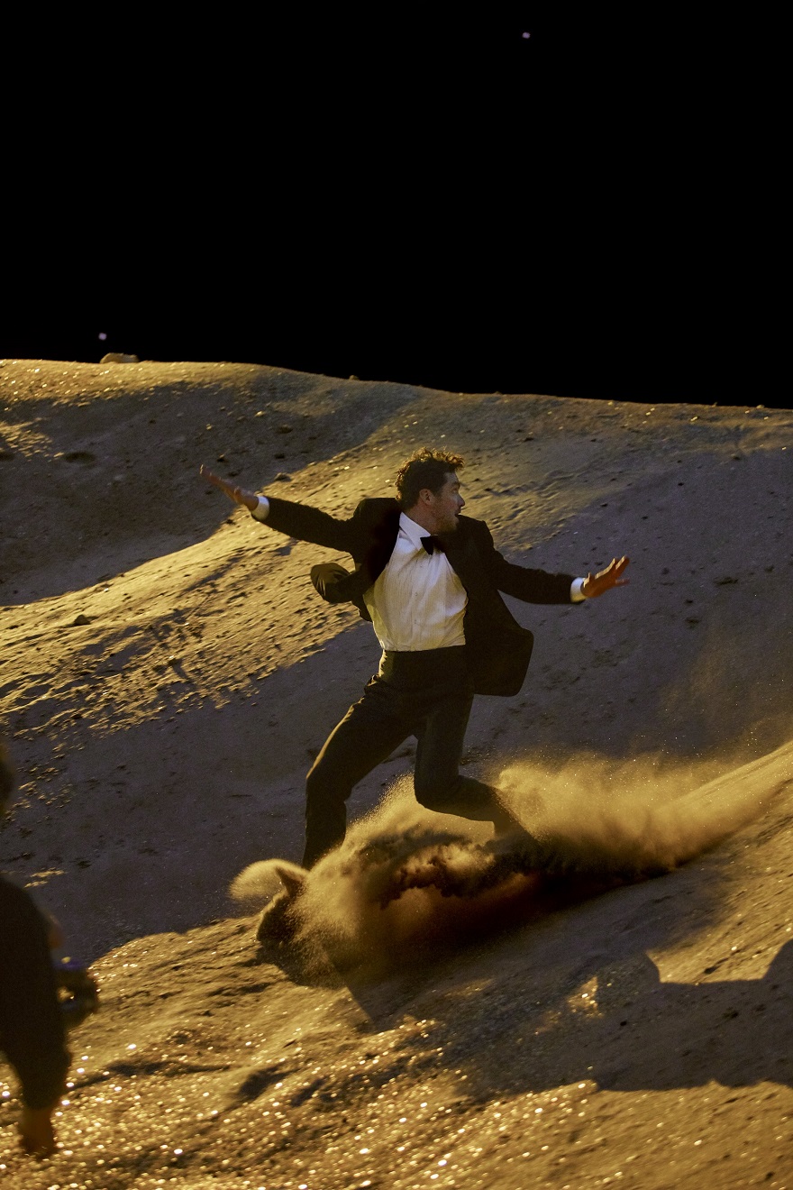 Άνδρας με σμόκιν τρέχει σε έδαφος που μοιάζει με τη Σελήνη